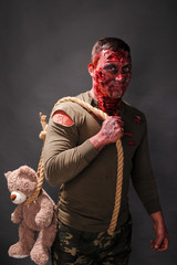 scary zombie with lacerations. blood. with a loop for the gallows in which a cute teddy bear is hung