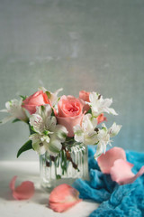 Peach Roses and White Alstroemeria arranged in a clear vase; White Table, Blue Accent Cloth; Neutral Background