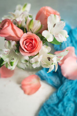 Peach Roses and White Alstroemeria arranged in a clear vase; White Table, Blue Accent Cloth; Neutral Background