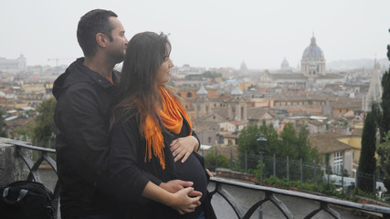 Fototapeta premium Man and pregnant woman caress belly and admire up view rome panorama, rainy day