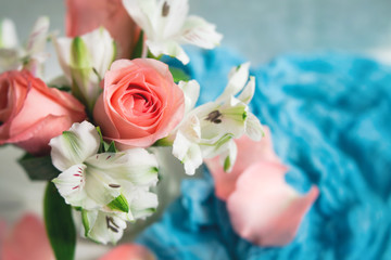 Peach Roses and White Alstroemeria arranged in a clear vase; White Table, Blue Accent Cloth; Neutral Background