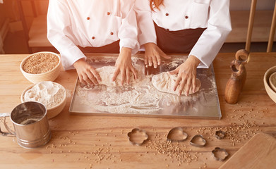 Children in cook uniform kneading dough on metal stand on table