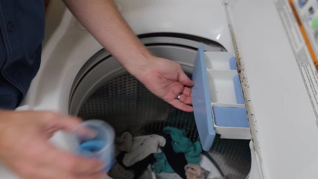 Hand pouring laundry detergent into washing machine dispenser