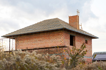 An unfinished brick house with a wooden roof frame is still under construction.