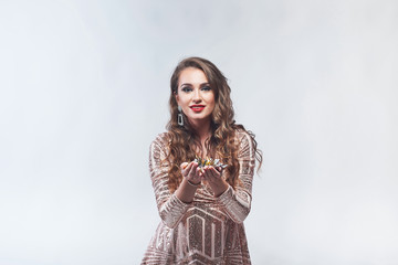 Young woman in elegant dress holding confetti in hands against white background.