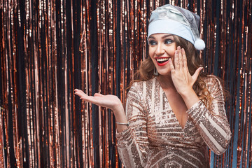 Obraz premium Portrait of young surprised woman in Santa hat looking aside at her hand holding something.