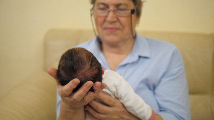 Grandmother hold newborn baby in her arms, child in focus, woman in background