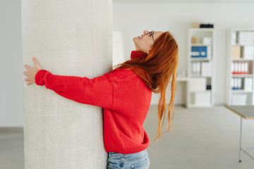 Exuberant young woman hugging an indoor pillar