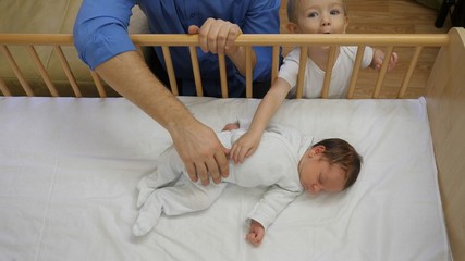 Detail of father hand and little brother caressing newborn baby sleeping in bed