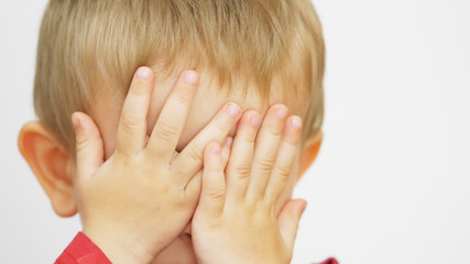 Portrait of funny child covering blue eyes, boy play hide and seek