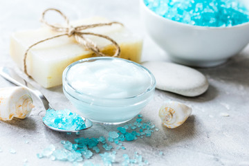Fototapeta na wymiar blue bath salt, body cream and shells for spa on gray table background