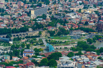 TBILISI, GEORGIA, JUNE 3, 2019: Aerial view from the Narikala fortress on the Tbilisi city, the capital of Georgia, full of small tiled roof houses, green trees, bridges over the Kura river