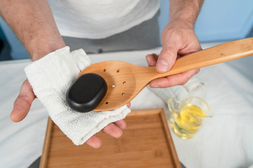 Close up on massage therapist at spa holding hot black basalt massage stone using bamboo spoon...