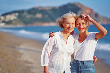 Fototapeta na wymiar Outdoor portrait of smiling happy caucasian senior mother with her adult daughter hugging and looking at the camera on sea beach.