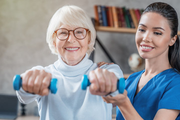 Old woman training with physiotherapist using dumbbells at home