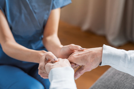 Assisting Senior People. Close Up Of Female Caregiver Holding Elderly Woman's Hands Indoors