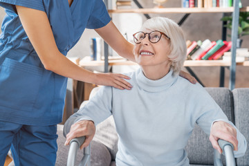 Cropped image of female caretaker helping senior woman to walk with walker at home