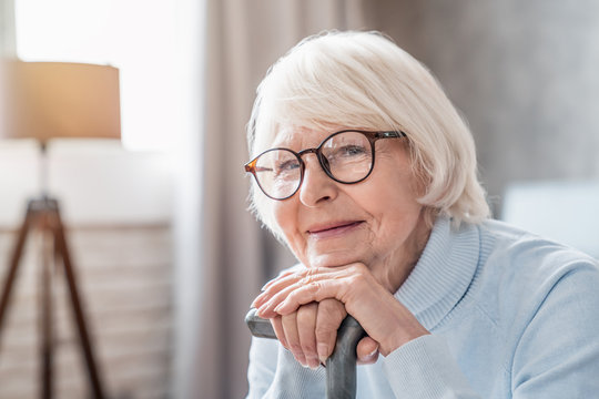 Close up of mature woman in glasses holding cane while sitting on sofa at home