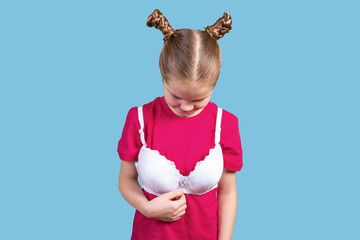 Little girl in mom's bra looking down. Isolated on a blue background.