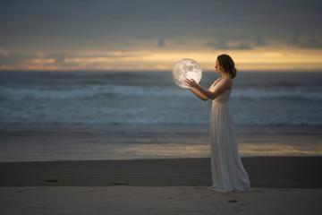 Astrology. Secret and riddle. Beautiful attractive girl on a night beach with sand hugs the moon,...