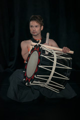 Japanese Taiko drummer with drum on a stage on a black background.