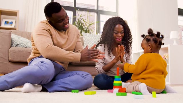 family, parenthood and people concept - happy african american mother, father and baby daughter playing with toy blocks at home