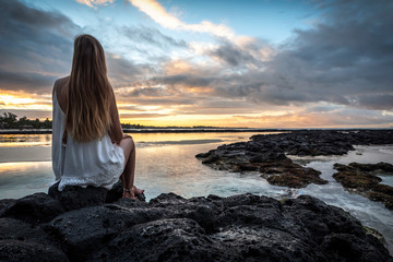 Junge Frau sitzt auf Felsen und schaut auf das Meer