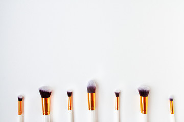 Flat lay top view of female cosmetics brushes set for makeup, are located at the bottom on white background. Cosmetics and beauty concept. Make up concept with space for text
