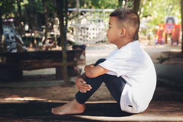 Asian kid lonely boy sitting in feel solitary sad mood at the park