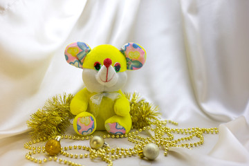 A yellow toy mouse next to Christmas balls on a beige background. Symbol of the new year 2020