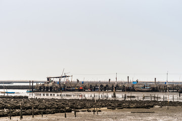 Ban Bai Bua, Thailand - March 16, 2019: Large Oyster beds and banks in the Gulf of Thailand during low tide. Silver sky. The pier with crane and strande boats.