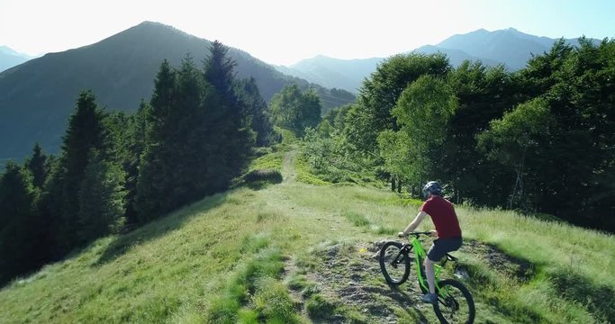 Biker riding mountain bike along forest trail aerial view in summer sunny day. Cross country biker. Aerial MTB bike riding on track trail. Riding mountain e-bike along path on the mountains