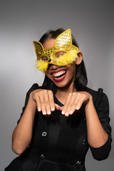 Portrait of attractive young Asian woman in gold cat carnival mask isolated over concrete wall background