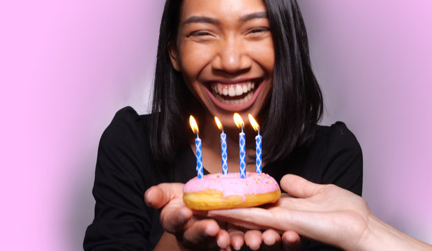 Pretty happy Asian girl blowing candle on birthday cake isolated over gray wall background