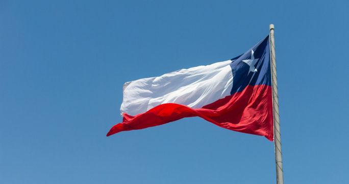 Flag of Chile flies in a strong wind against a bright blue sky with sun glare