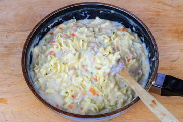 Tuna Pasta Alfredo hot from the stove in skillet with mixing spoon sitting on wooden cutting board.