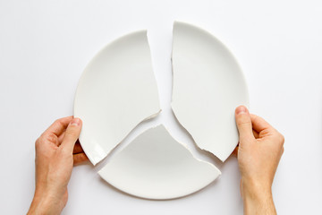 Top view of man hands holding a broken white plate. Metaphor for divorce, relationships, friendships, crack in marriage. Love is gone. Isolated on white background