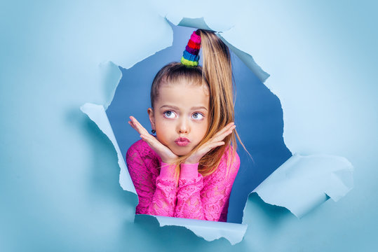 Thoughtful little girl seven years old is looking away on copy space. Interested minded kid touching chin, thinking on a blue background, Funny kid pout lips. Conceived some kind of prank, concept