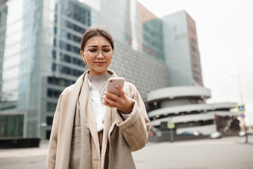 Beautiful Asian girl with glasses discontentedly typing a text message on her smartphone