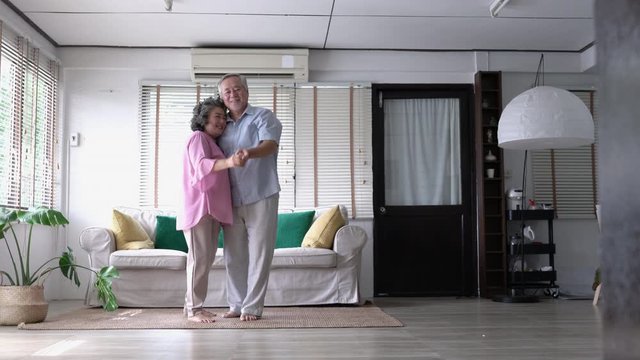 Happy asian mature senior couple dancing laughing in living room at home. Beautiful romantic middle aged older grandparents relaxing fun together celebrating anniversary enjoy care love tenderness.