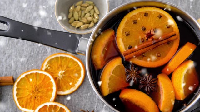 christmas and seasonal drinks concept - snowing over pot with hot mulled wine, orange slices and aromatic spices on grey background