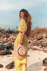 cheerful young stylish woman in elegant dress outdoors wearing hat havinf fun at sunset