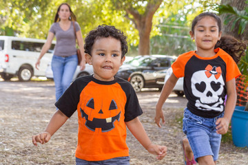 Kids run ahead of Mom in the country excited about the pumpkin patch. The siblings are wearing Halloween t-shirts as they as Mom tries to keep up.