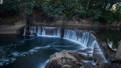 Panoramic View of a Man-Made Waterfall on a River - in a Secluded Spot in the City, Surrounded by Lush Green Trees