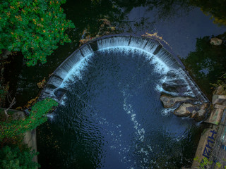 Aerial, Top-Down View of a Man-Made Waterfall on a River - in a Secluded Spot in the City, Surrounded by Lush Green Trees