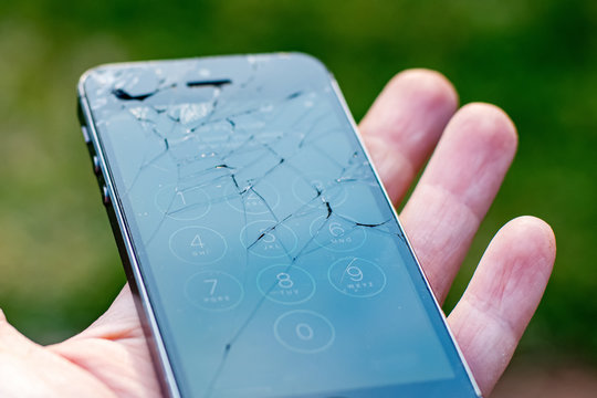 Hand holding working smartphone with badly smashed screen. Cracked display needs repair