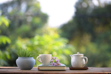 white cup with teapot and small plant with purple daisy flower and book on wooden table