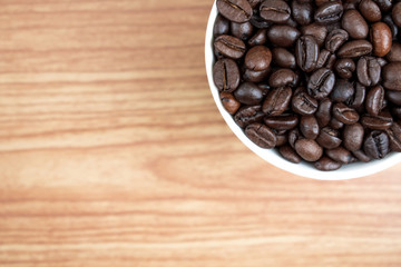Coffee beans in a white mug on an old brown wood texture background. With copy space.