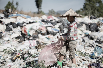 A poor boy collecting garbage waste from a landfill site in the outskirts .  children work at these sites to earn their livelihood. Poverty concept.