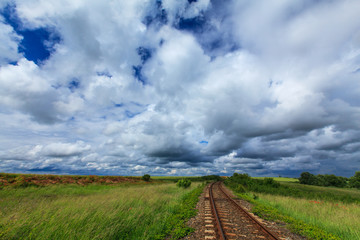 Old railroad in remoter rural area in Europe on a summer day, under a sky covered with storm clouds